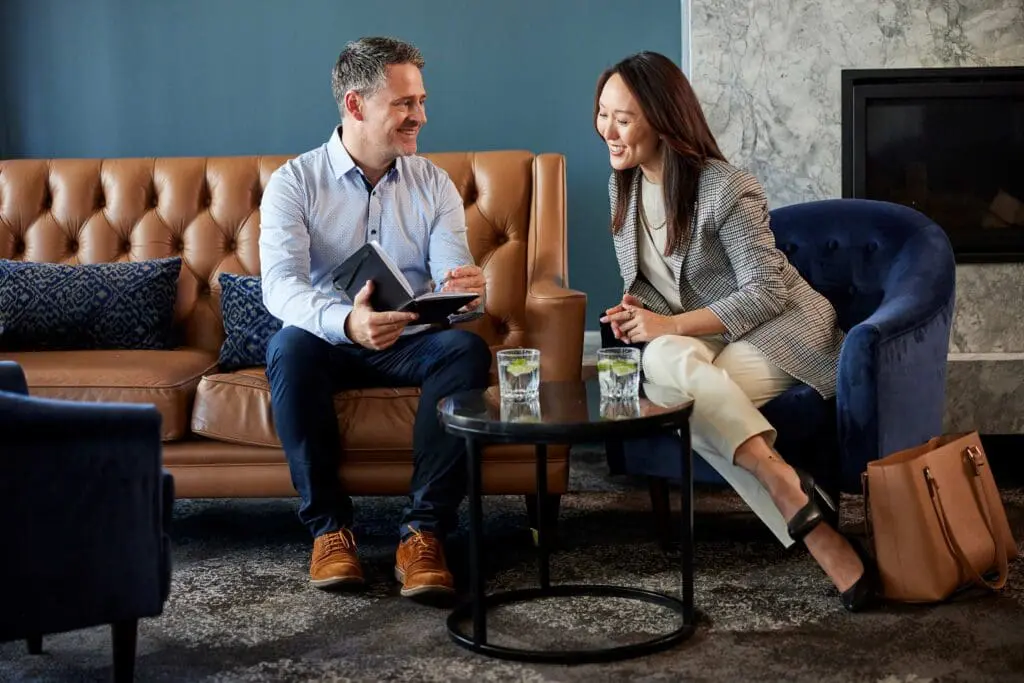 Commercial photography of two business professionals sitting in leather armchairs chatting over coffee in a hotel lounge.