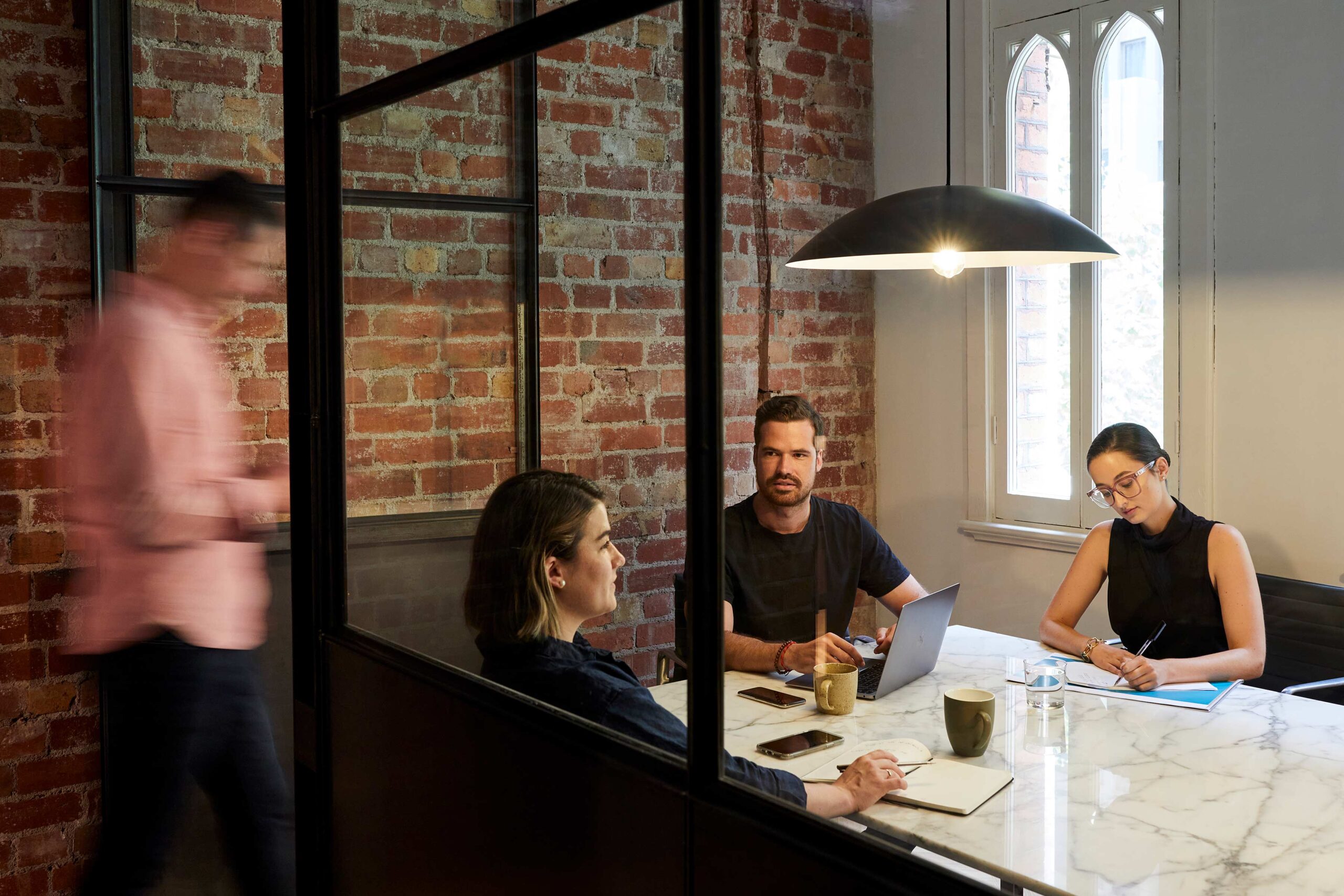 Office workers and a team meeting around a table and a man walks into The Door