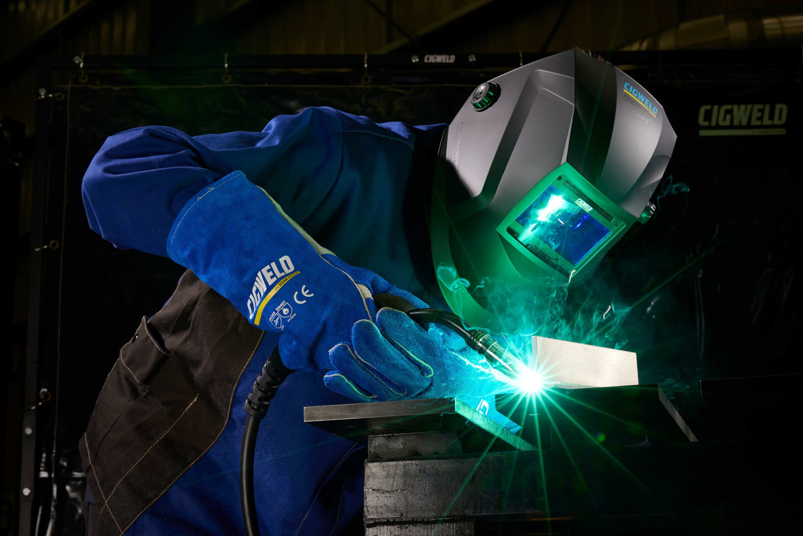 A welder work on a piece of metal at workbench with full protective gear on, including a helmet on a construction site.