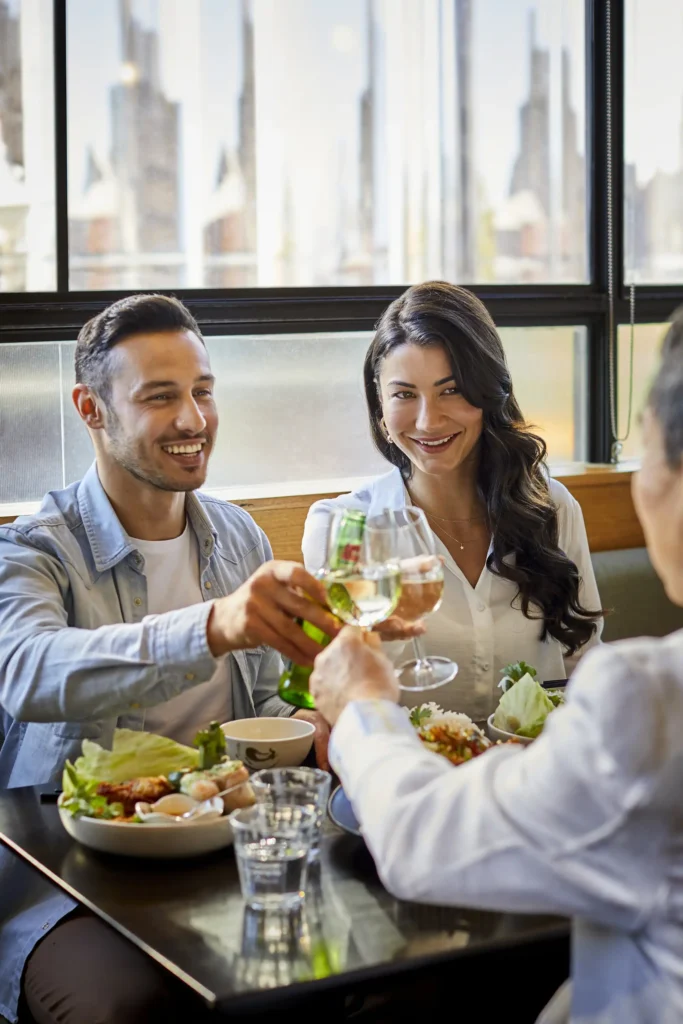 A couple eats a  meal together with family and toast their drinks across the table