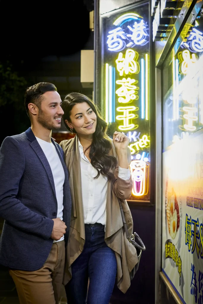 A young Graham couple looks into a shot window with Chinese neon lights around them