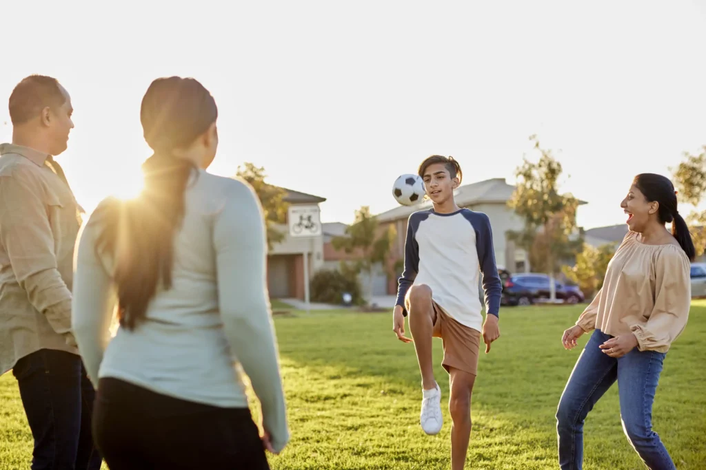 Lifestyle image of a family playing soccer in the park with the sunset coming down behind them